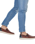 Man in jeans wearing brown leather boat shoes with navy accents, cream midsole and brown outsole.