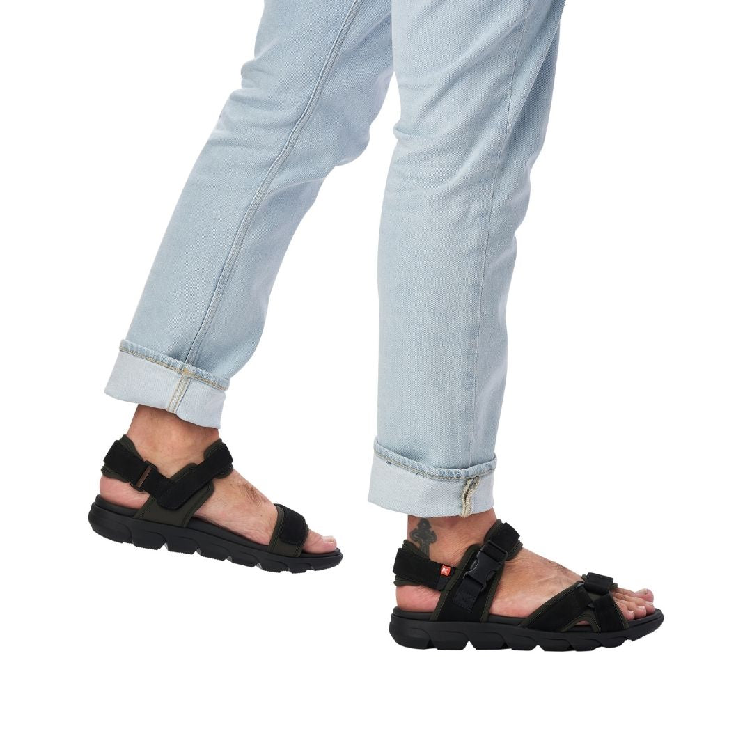 Man in jeans wearing black sport sandal with three straps of adjustability 