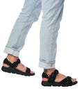 Man in jeans wearing black sport sandal with three straps of adjustability 