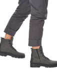 Man in grey pants wearing grey combat style winter boots with lace closure and outside zipper.