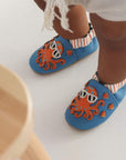 Baby wearing blue leather shoes with orange octopus and fish on them.