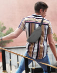 Man in striped shirt wearing a grey fanny pack as a crossbody bag. Bag has zippered closure and Travelon emblem on front.