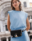 Women in blue dress wearing a black belt bag with floral print. Gold Travelon logo emblem is on the front flap.