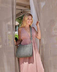 Women in a pink dress is wearing a grey quilted Travelon crossbody bag.