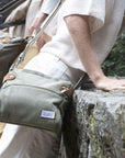 Women wearing olive green canvas crossbody bag with top and front zipper. Patch on front with Travelon logo on it.