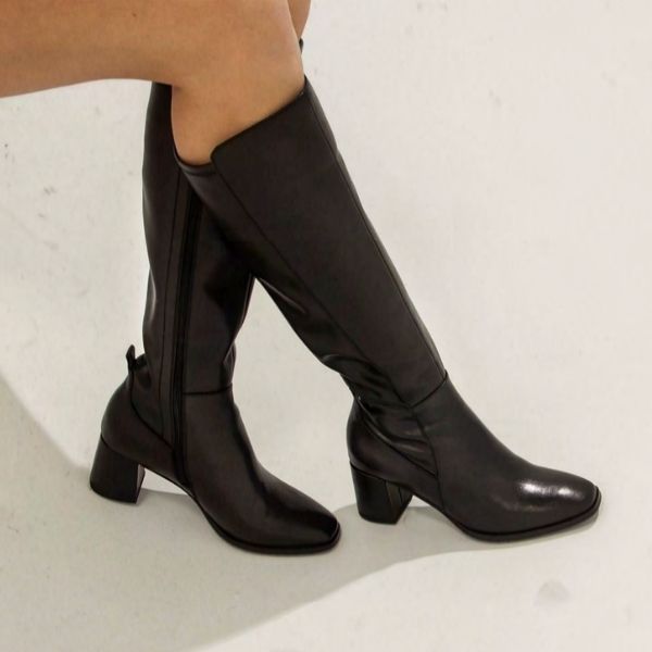 Women with crossed legs wearing the tall black leather Blondo boot with leather covered heel.