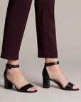 Women in purple pants wearing black leather heeled dress sandal with adjustable ankle strap.