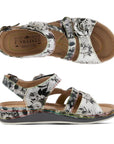 Top and side view of black and white backstrap sandal with floral details. L'Artiste logo is printed on insole.