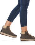 Women in jeans wearing grey sneaker boot with faux fur cuff and beige outsole.