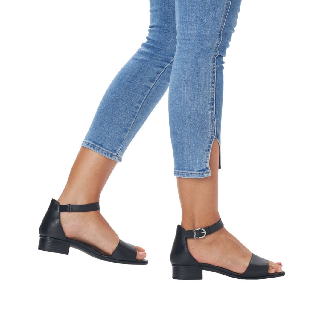 Light denim wearing black sandal that has ankle strap with silver buckle and low stacked heel.