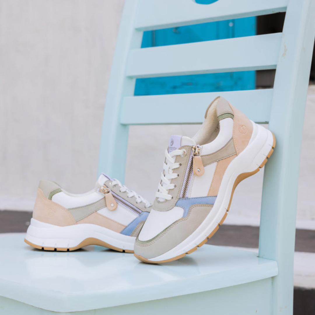 White, pale pink, blue and green sneaker with white laces and side zipper closure sitting on a blue chair.