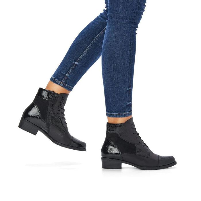 Legs wearing black and black patent patchwork ankle boot with lace closure.