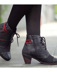 Legs in black tights wearing black booties with laces, red accents and polka dot details.