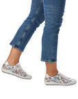 Legs in jeans wearing blue floral lace up shoe with zipper side closure and grey midsole.