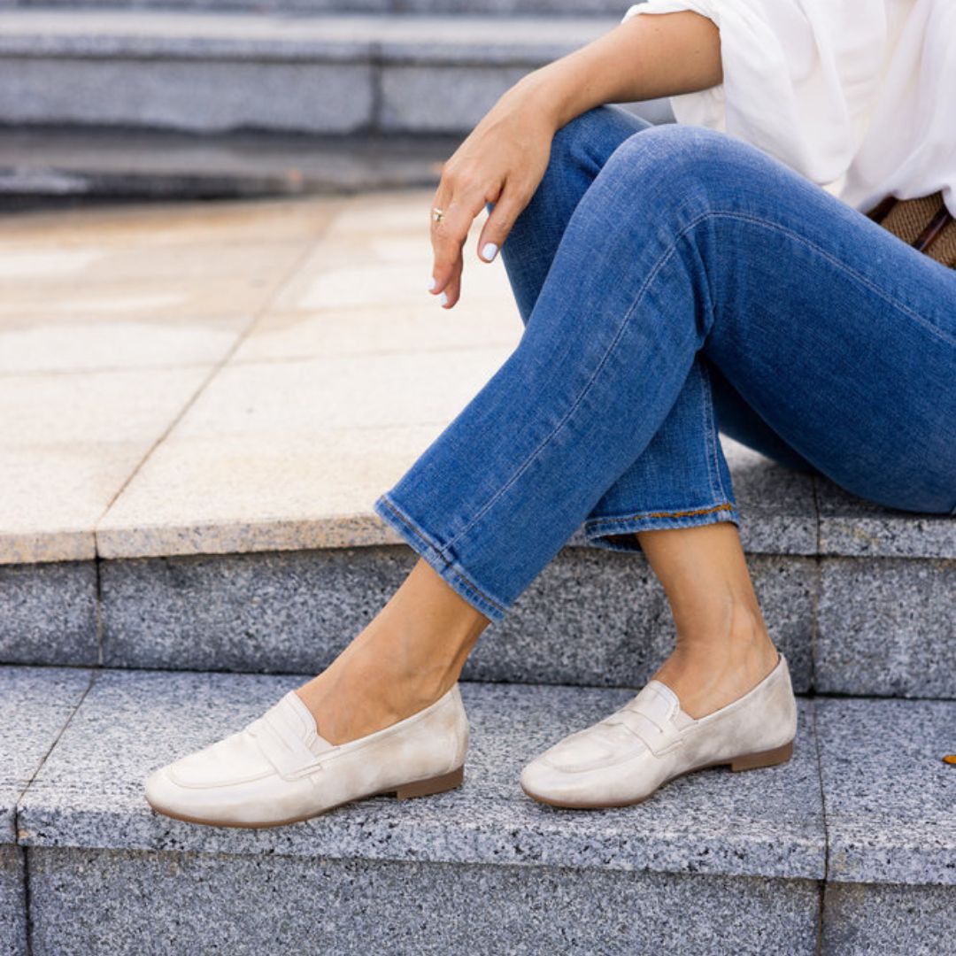 Women in jeans wearing gold penny loafer with brown outsole.