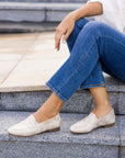 Women in jeans wearing gold penny loafer with brown outsole.