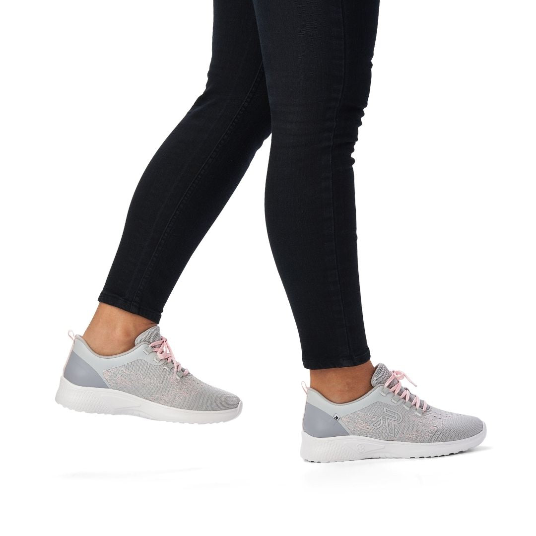 Women in jeans wearing a grey and pink mesh sneaker with pink laces and white outsole.