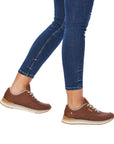 Women in jeans wearing brown leather sneaker with white laces. R-Evolution logo tag on side and tongue.