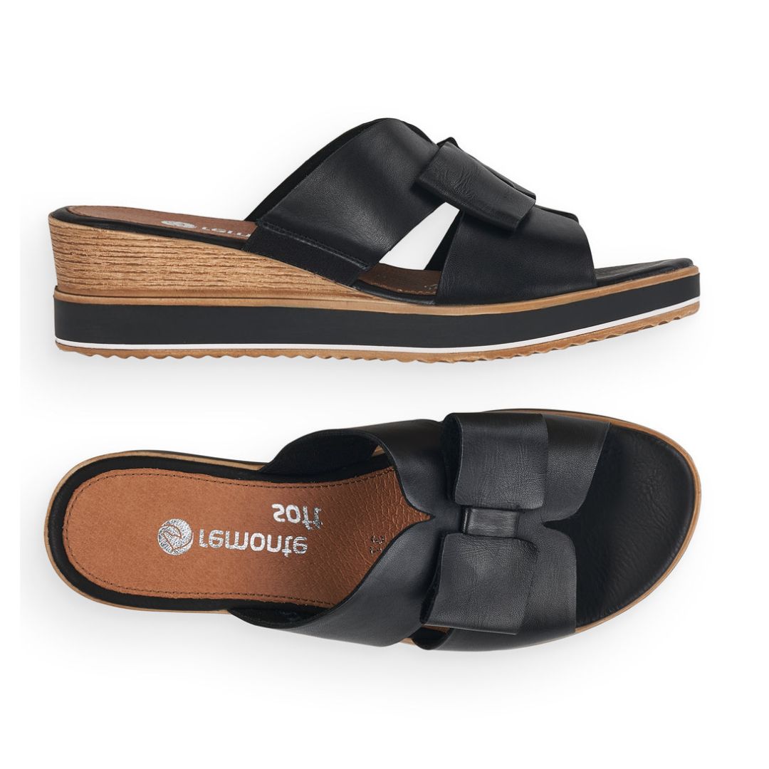 Top and side view of black leather slide wedge sandal with bow. Remonte logo printed on brown insole.