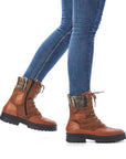 Women in jeans wearing brown lace up boot with yarn knit cuff, inside zipper and black outsole.