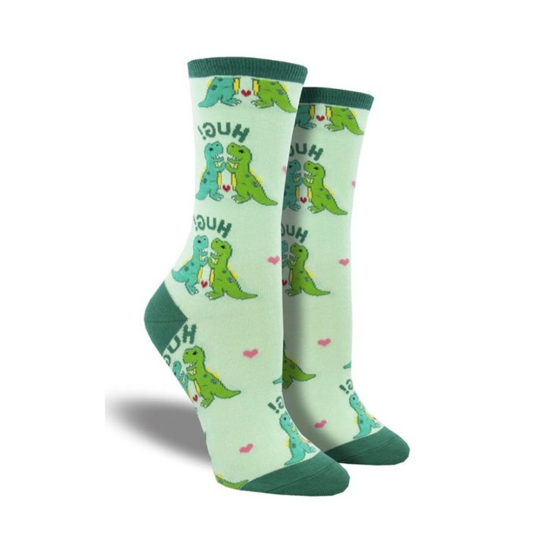 Women's Socksmith Hugs Socks featuring green cartoon dinosaurs hugging with 'HUGS!' text on light green cotton crew socks. Fun dinosaur print for casual wear.