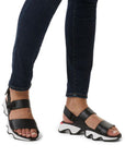 Legs in dark jeans wearing black leather sandals with a backstrap and thick wavy white and black oustole.