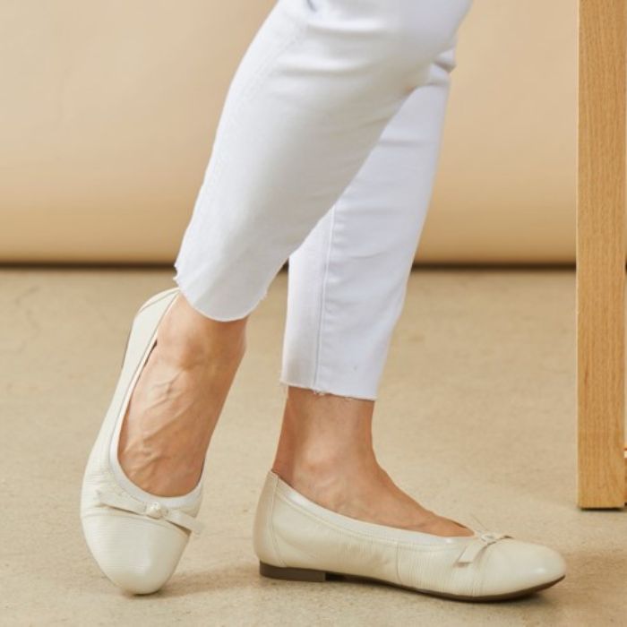 Women in white pants wearing white ballerina flat with bow on toe.