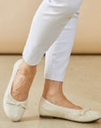 Women in white pants wearing white ballerina flat with bow on toe.