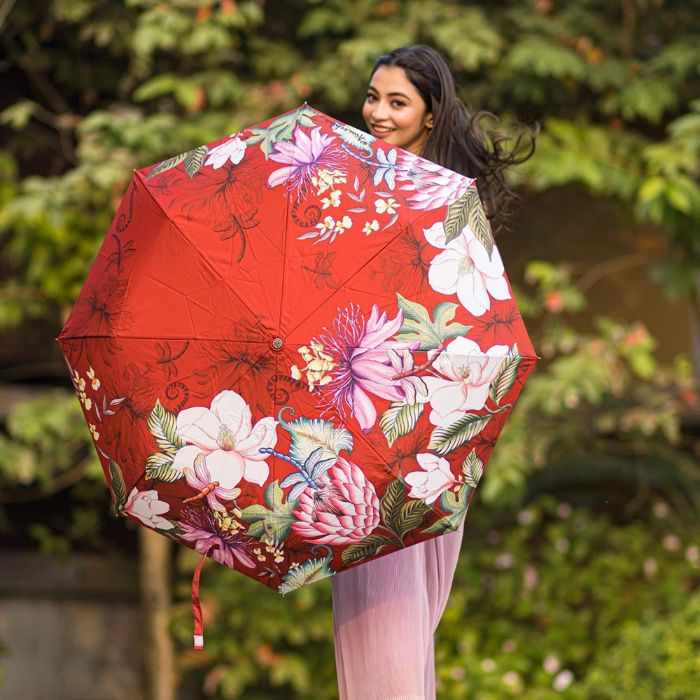 Women in pink dress holding red floral pattern umbrella.
