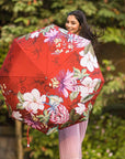 Women in pink dress holding red floral pattern umbrella.