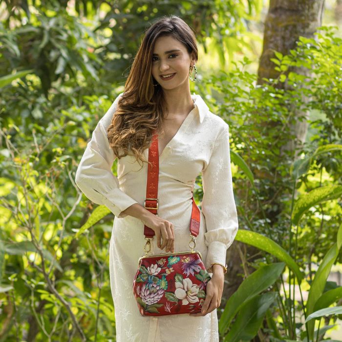 Women wearing a red satchel with hand painted floral and dragonfly design. This bag features a gold clasp closure and crossbody strap.